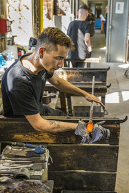 France, Moselle (57), Meisenthal, Centre international d’Art verrier (CIAV), l'atelier de soufflage, le verrier Nicolas régularise la masse au marbre tout en effectuant une rotation continue de sa canne et préparation de la paraison avant le passage au moule