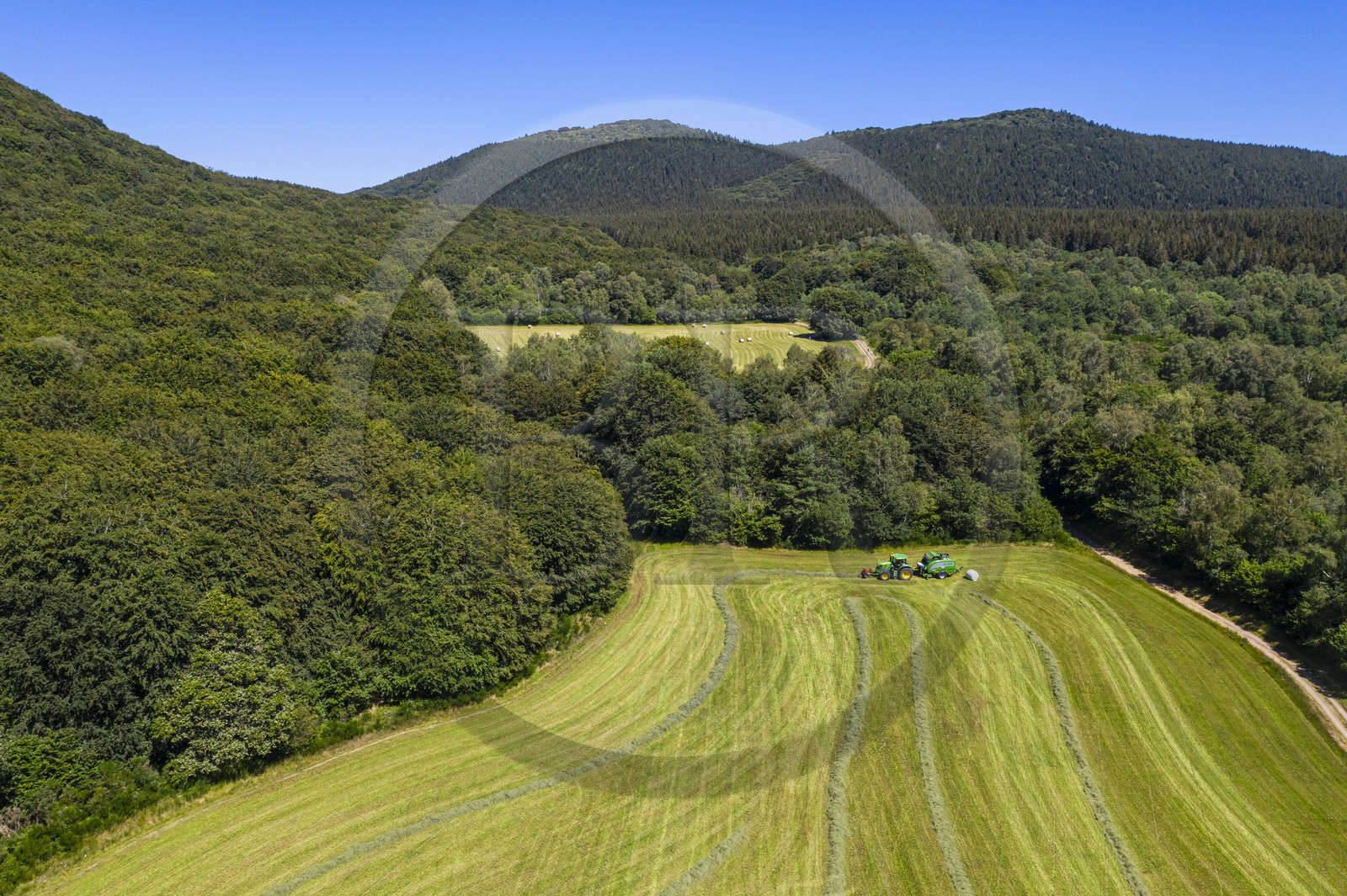 France, Puy-de-Dôme (63), Saint-Ours-les-Roches, hameau de Beauregard, tracteur récoltant le fourrage avec une presse enrubanneuse de balles de foin dans un champ (vue aérienne)