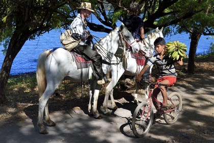 Nicaragua, Ometepe Island in Lake Nicaragua, riders along the lake and young cyclist carrying a bunch of bananas