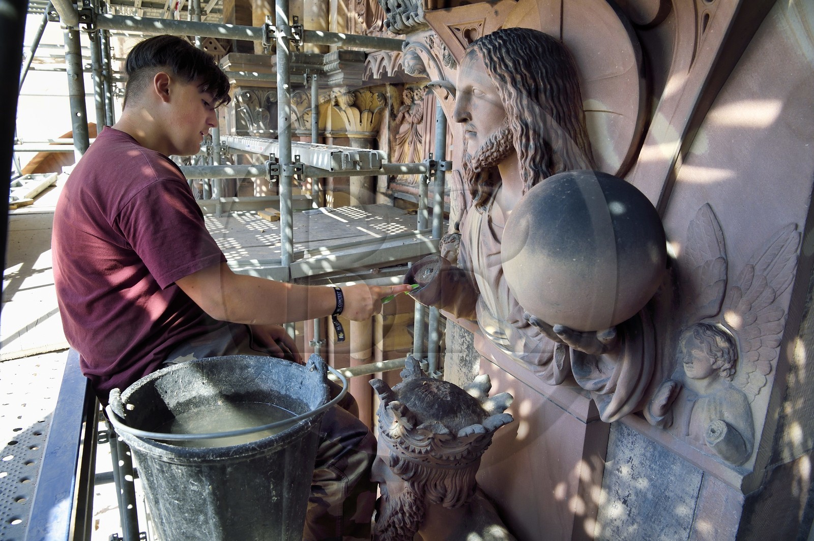 France, Bas-Rhin (67), Strasbourg, vieille ville classée au Patrimoine Mondial de l'UNESCO, la cathédrale Notre-Dame, chantier de restauration du Portail du Jour du jugement, Christ redempteur au dessus du Roi Salomon, nettoyage de la sculture à la brosse à dent par un apprenti tailleur de pierre