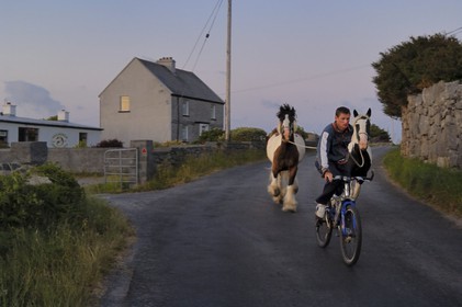 Irlande, Comté de Galway, Aran Islands, Inishmore, retour de nuit à bicyclette en tenant ses deux chevaux