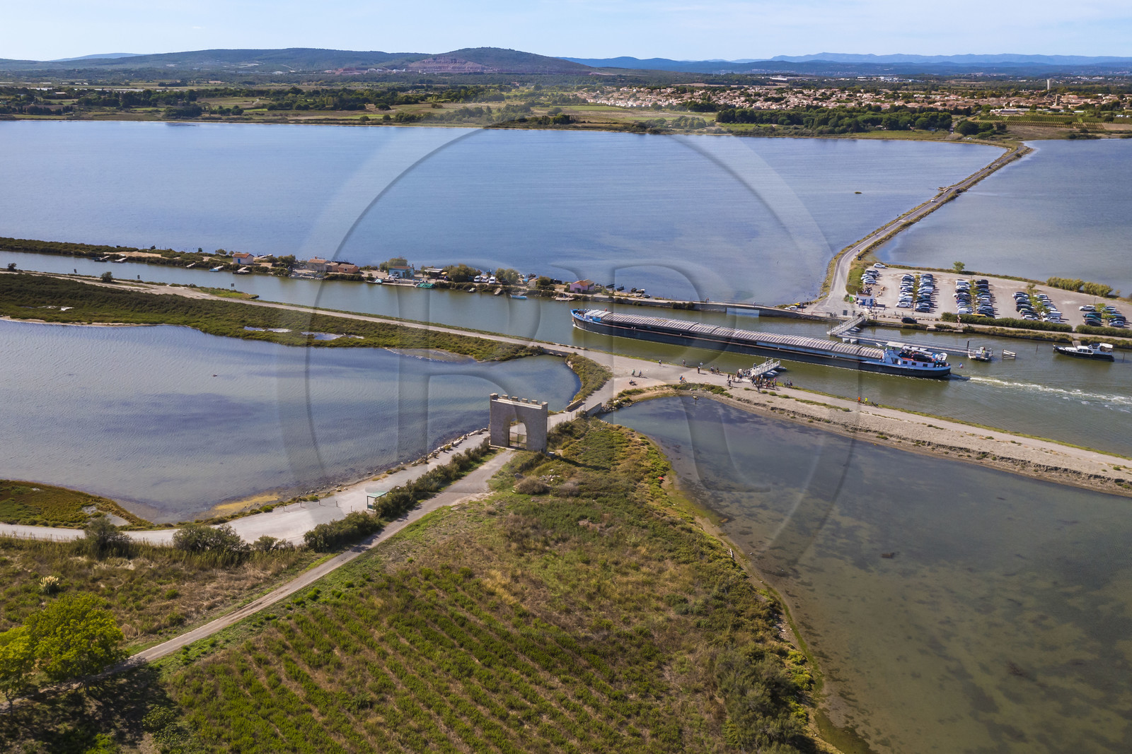 France, Hérault (34), Villeneuve-lès-Maguelone (Palavas-Les-Flots), péniche sur le canal du Rhône à Sète passant la Passerelle du Pilou devant la Porte de Maguelone sur l'Ile de Maguelone, Villeneuve-lès-Maguelone en arrière plan (vue aérienne) France, Herault, Villeneuve les Maguelone (Palavas Les Flots), barge on the Rhone to Sète Canal passing the Passerelle du Pilou in front of the Porte de Maguelone on the Ile de Maguelone, Villeneuve les Maguelone in the background (aerial view)