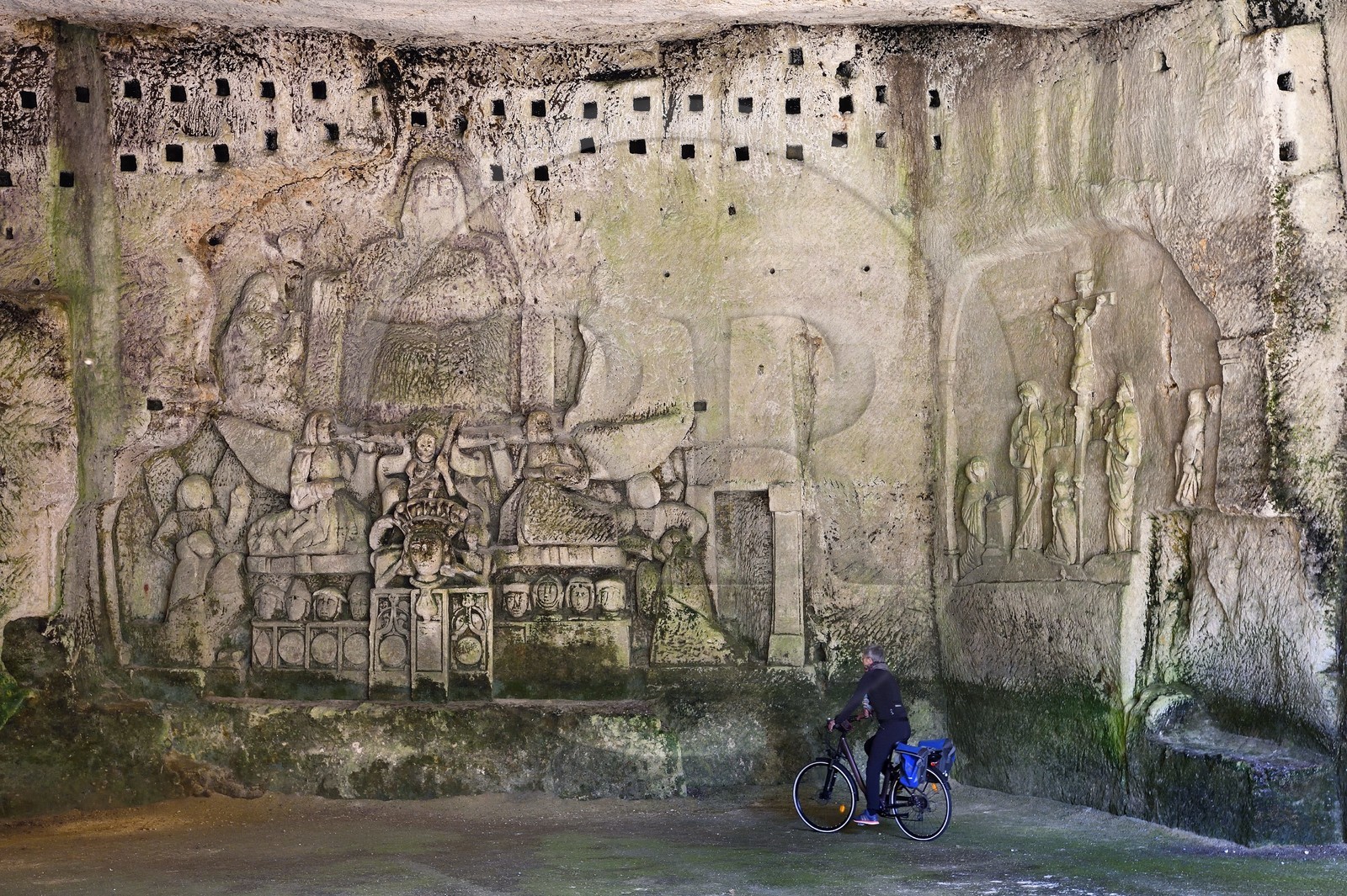 France, Dordogne (24), Brantôme, l'abbaye bénédictine Saint-Pierre de Brantôme, vestiges du premier monastère troglodytique aménagé dans les grottes au pied de la falaise avec notamment dans la grotte du Jugement Dernier, à droite la Crucifixion du début XVIIème siècle, à gauche un bas relief du XV ème siècle sous le pigeonnier, cycliste sur la véloroute la Flow Vélo