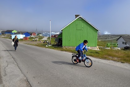 Groenland, cote ouest, Ile de Disko, maisons du village de Qeqertarsuaq et icebergs en arrière plan, enfant à bicyclette