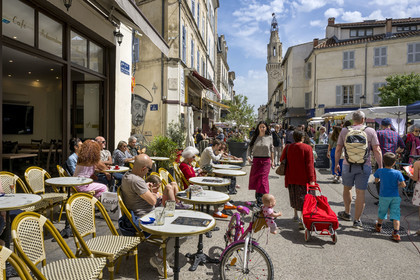 France, Vaucluse (84), Avignon, terrasses de café sur la place du Portail Matheron un jour de marché, un portrait de Raimu lors de la partie de cartes du film Marius de Marcel Pagnol par l'artiste graffeur Lekto, le clocher des Augustins en arrière plan