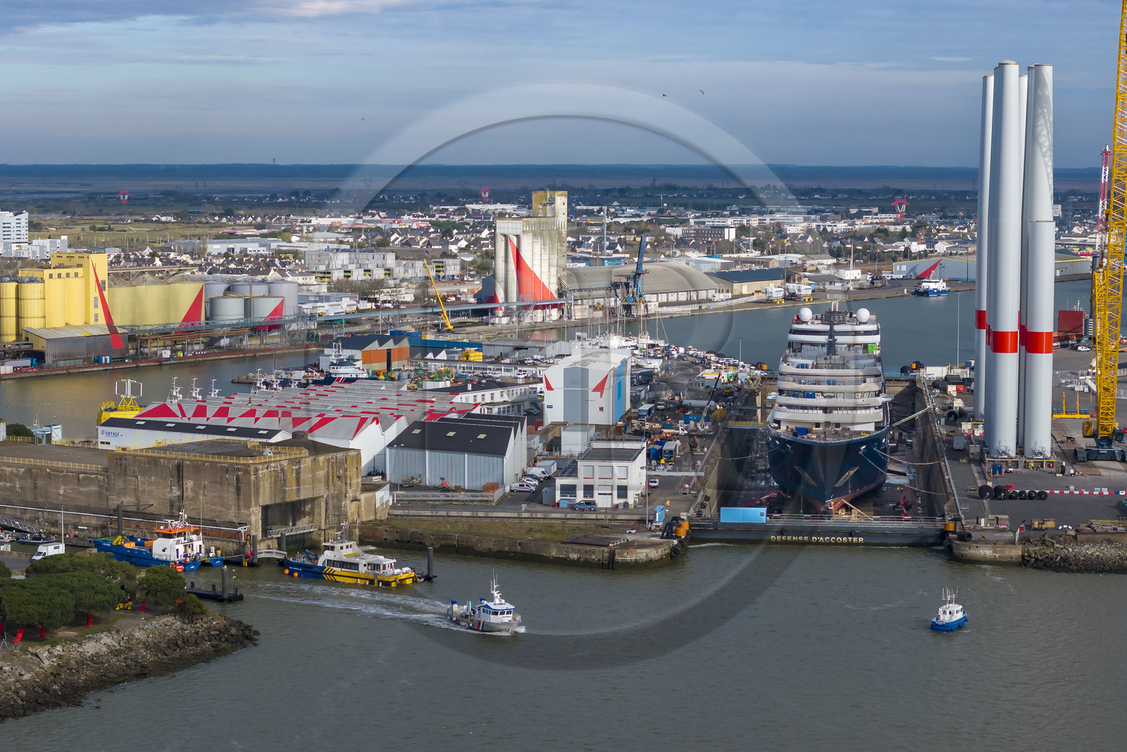 France, Loire-Atlantique, Saint-Nazaire, the fortified lock of the former German submarine base built during the last world war on the left and the construction site of the luxury super-yacht Ritz-Carlton Luminara in the Joubert dry dock on the right, the wind turbine towers are stored before embarkation (aerial view)