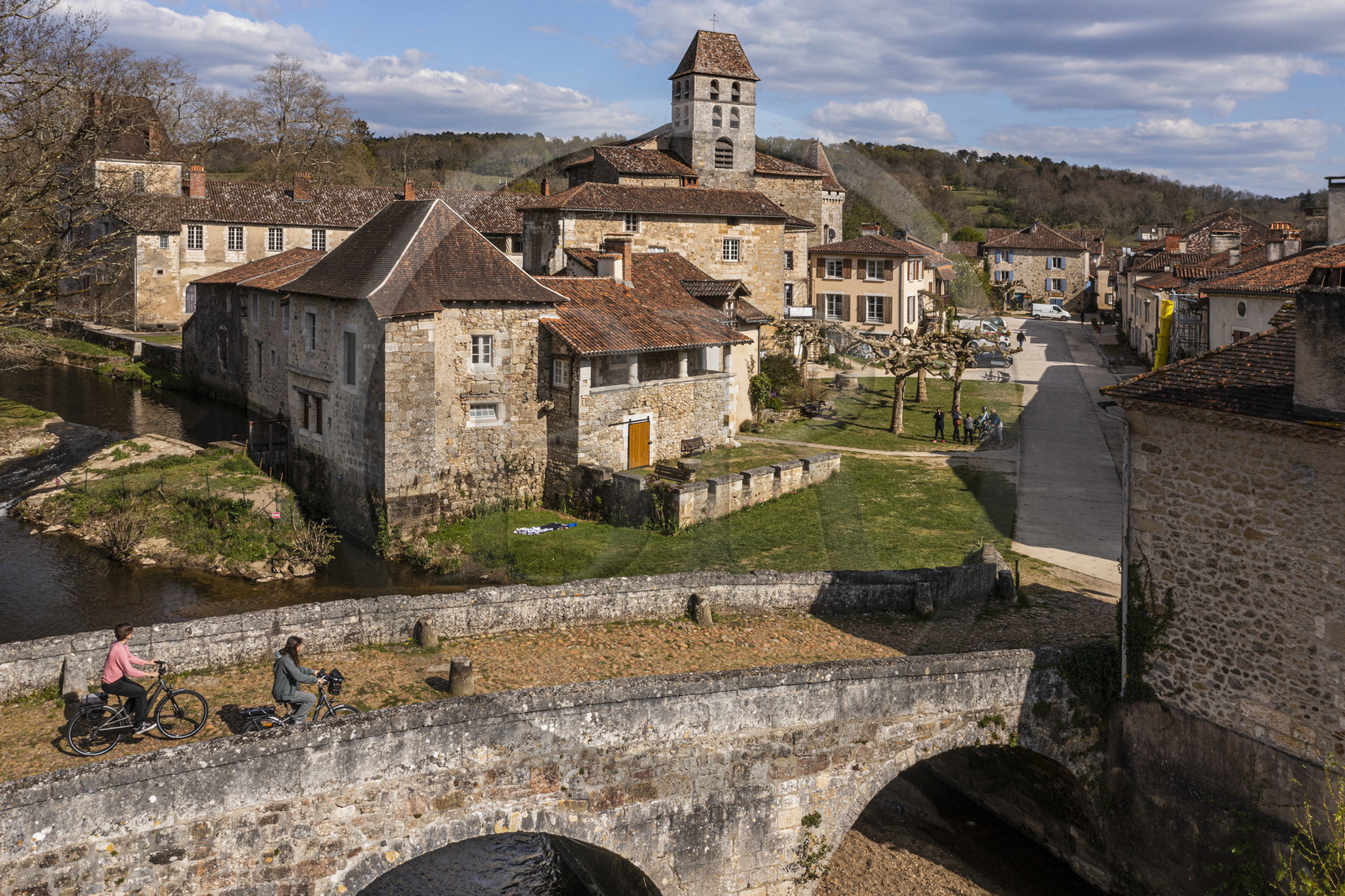 France, Dordogne, Périgord Vert, Saint Jean de Cole, labelled Les Plus Beaux Villages de France (The Most Beautiful Villages of France), cyclists on the Flow Vélo cycle route crossing the medieval bridge of the 12th century, the St. John the Baptist (Saint-Jean-Baptiste) church bell tower (aerial view)