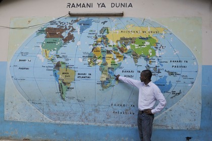 Tanzanie, Dar es-Salaam, Joseph Malumbo pointe la Tanzanie sur la mappemonde murale dessinée sur le mur d'entrée de son ancienne école du quartier de Kivukoni