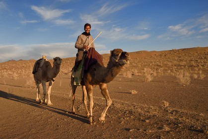 Iran, Isfahan province, Dasht-e Kavir desert, Mesr in Khur and Biabanak County, man riding his camel in the desert at sunset