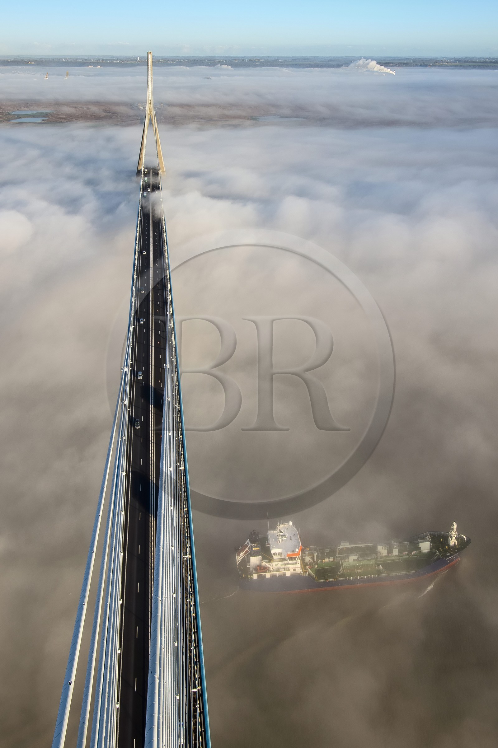 France, between  Calvados and Seine Maritime, cargo passing under the Pont de Normandie (Normandy Bridge) that emerges from the morning mist of autumn and spans the Seine, the Natural Reserve of the Seine estuary in the background, view from the top of the south pylon