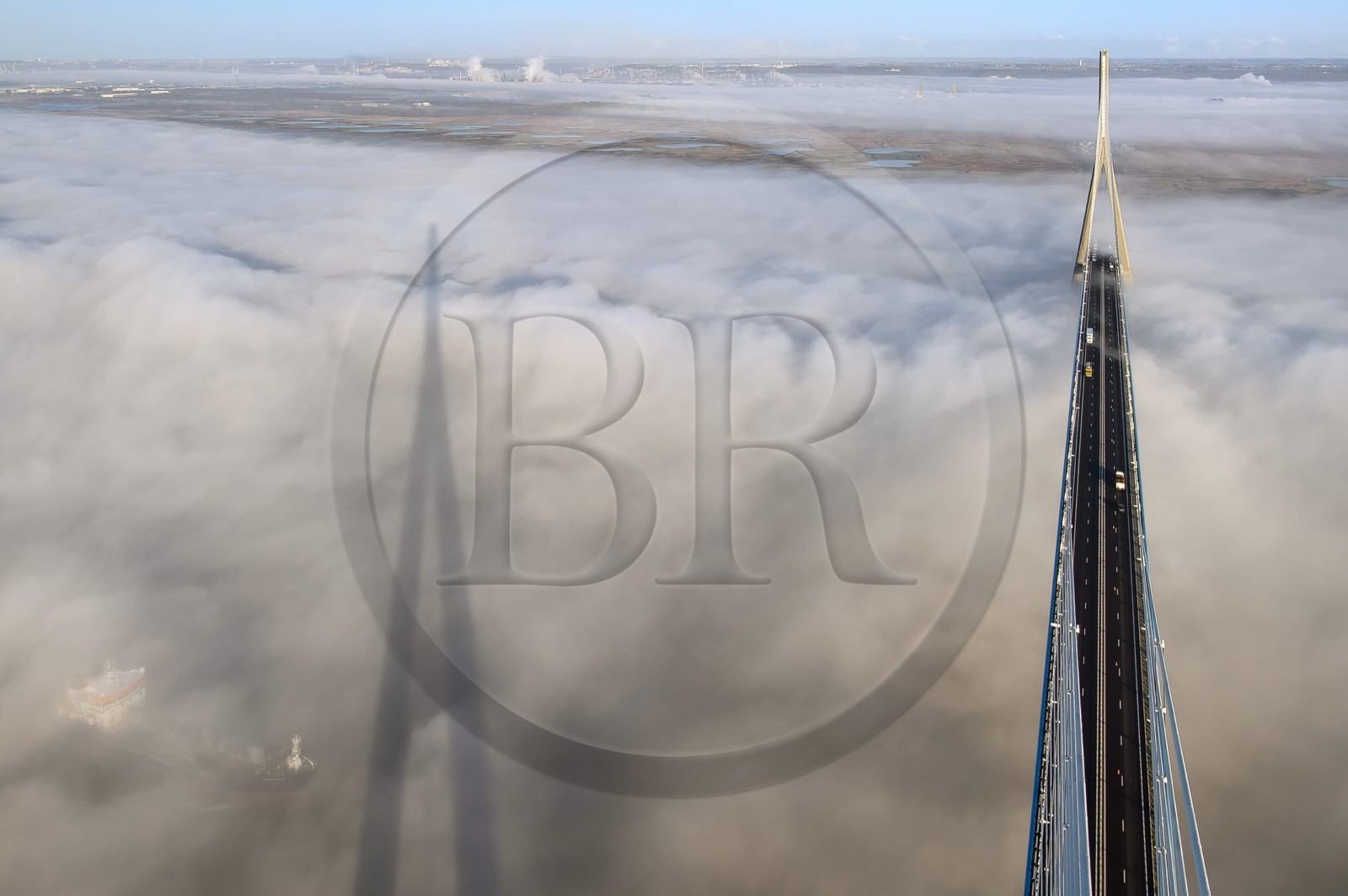 France, between  Calvados and Seine Maritime, cargo passing under the Pont de Normandie (Normandy Bridge) that emerges from the morning mist of autumn and spans the Seine, the Natural Reserve of the Seine estuary in the background, view from the top of the south pylon