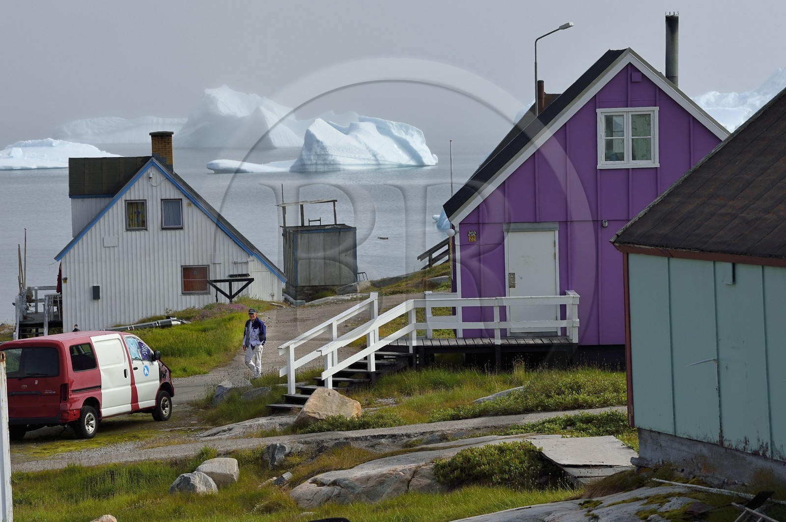 Groenland, cote ouest, Ile de Disko, maisons du village de Qeqertarsuaq et icebergs en arrière plan