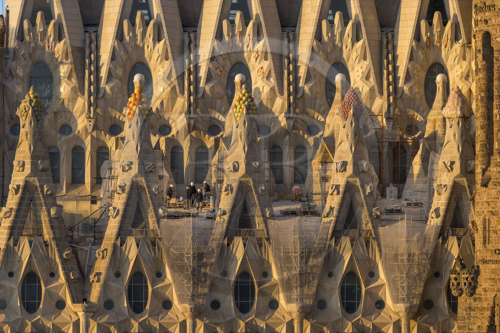Spain, Catalonia, Barcelona, Eixample district, Sagrada Familia basilica by Catalan modernist architect Antoni Gaudi, listed as a UNESCO World Heritage Site, peaks topped with mosaics in the shape of fruits surrounding the construction site on the roof of the nave here on the Passion facade side