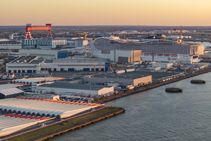 France, Loire-Atlantique (44), Saint-Nazaire, les tours d'éoliennes et les pales sont stockées avant embarquement, le paquebot de 333m MSC World America construit par les Chantiers de l'Atlantique en arrière plan (vue aérienne)