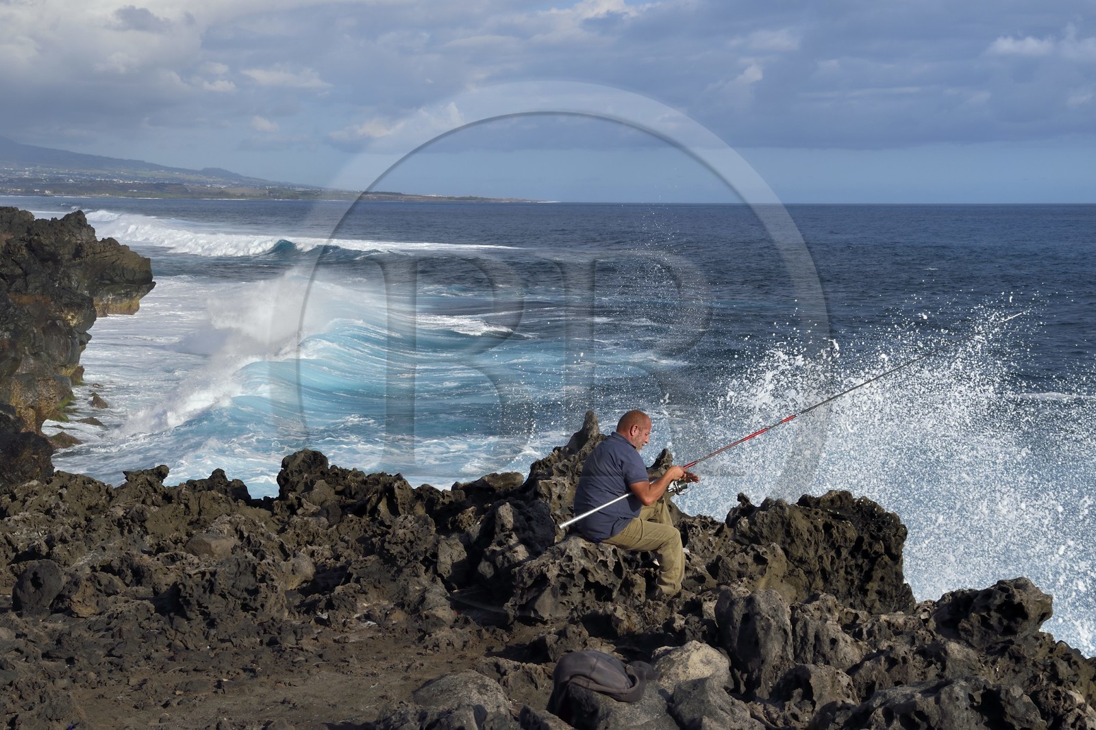 France, Ile de la Reunion, L'Etang Salé les Bains, la côte entre Le Gouffre et l'Etang du Gol, roches noires basaltiques d'origine volcanique tourmentées par l'océan, pêcheur à la ligne