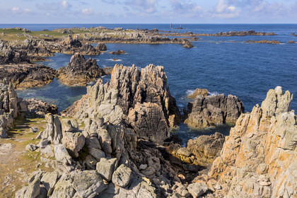 France, Finistère (29), Mer d'Iroise, Ile d'Ouessant, rochers façonnés par les tempêtes au pied du phare du Créac’h, le phare de Nividic sur la Pointe de Pern en arrière plan (vue aérienne)