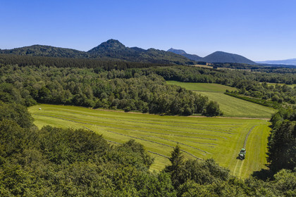France, Puy-de-Dôme (63), Saint-Ours-les-Roches, hameau de Beauregard, tracteur récoltant le fourrage avec une presse enrubanneuse de balles de foin dans un champ, en arrière plan le volcan le Puy Chopine à gauche et le Puy de Dome à droite (vue aérienne)
