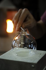 France, Moselle (57), Meisenthal, Thibaut souffleur au Centre international d’Art verrier (CIAV), fabrication d'une boule de Noël en verre. Une petite dentelle de verre tournée autour d’une petite baguette en fer va faire office d’attache qui est scellée à chaud
