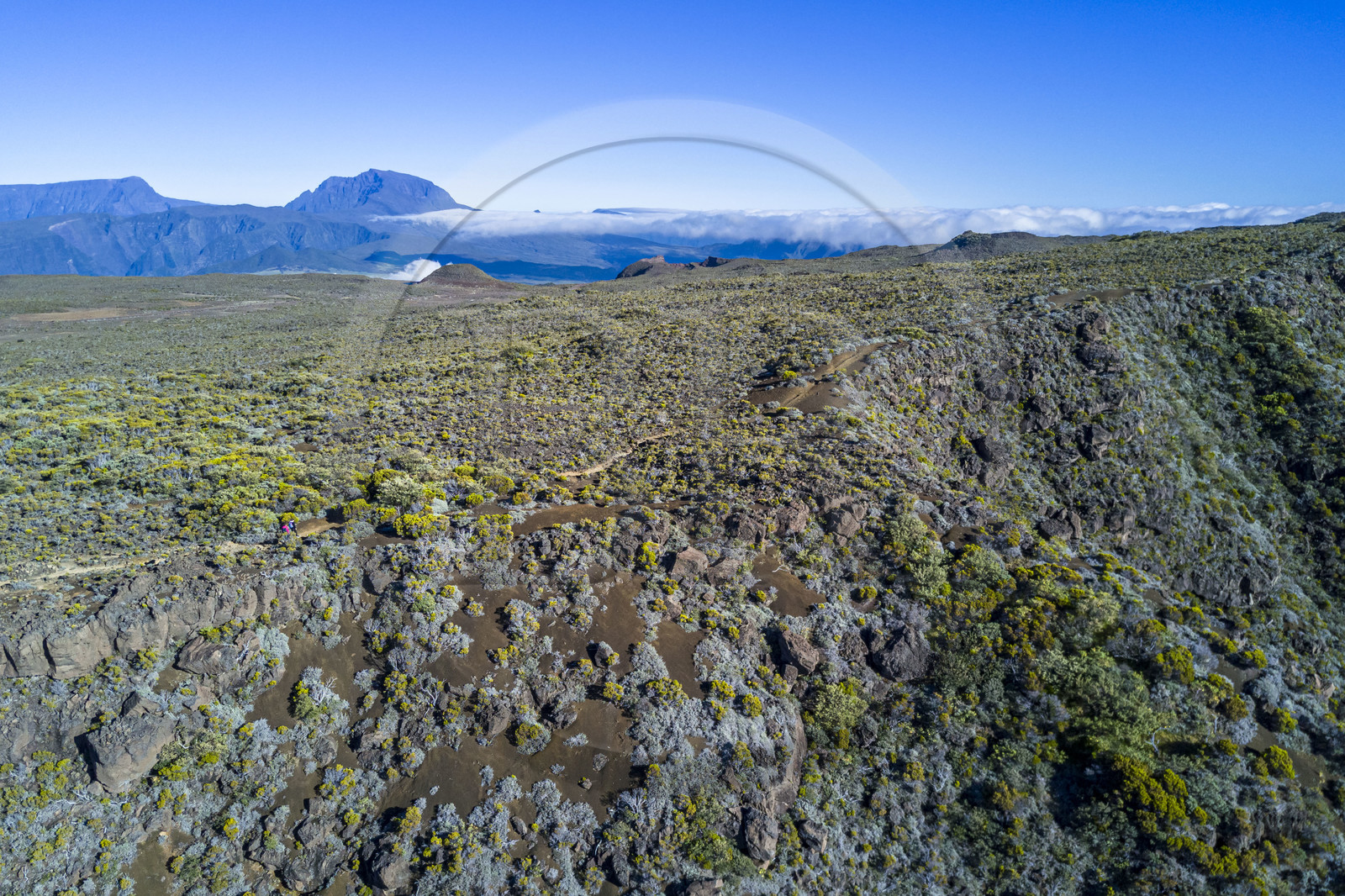 France, Ile de la Reunion, Parc National de la Réunion classé Patrimoine Mondial de l'UNESCO, sur les pentes du volcan de Piton de la Fournaise, randonneur sur le sentier de l'oratoire Ste Thérèse au dessus de la Plaine des Sables, le Piton des Neiges en arrière plan au nord (vue aérienne)