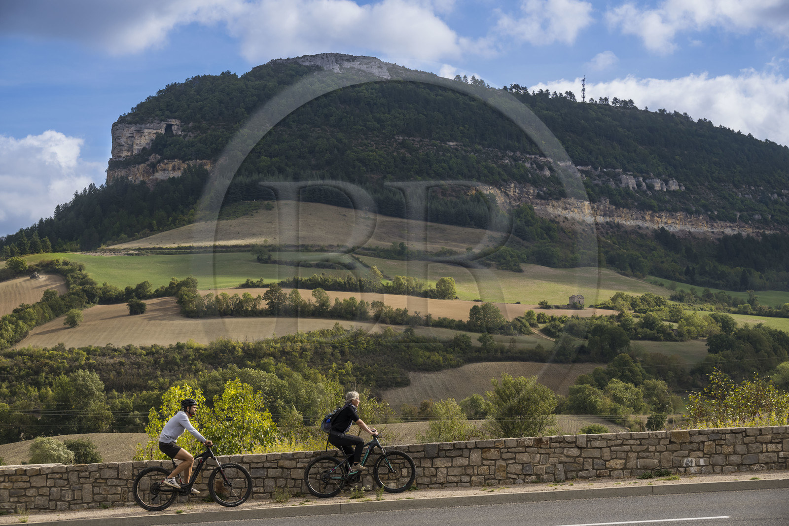 France, Aveyron (12), parc naturel régional des Grands-Causses, Roquefort-sur-Soulzon, cyclistes effectuant l'itinéraire cyclo touristique Brebis'Cyclette en Pays de Roquefort, le rocher du Combalou abritant les fleurines des caves de Roquefort en arrière plan