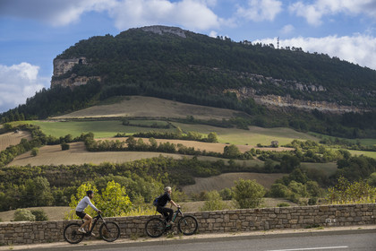 France, Aveyron, Grands-Causses Regional Nature Park, Roquefort sur Soulzon, cyclists on the Brebis Cyclette tourist cycle route in the Pays de Roquefort, the rock of Combalou sheltering the fleurines of the Roquefort cellars in the background