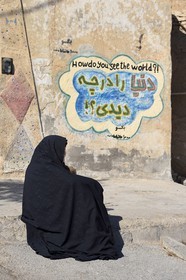 Iran, Isfahan province, Dasht-e Kavir desert, city of Nain also known as Naein, woman in front of a house with graffiti showing how do you see the world