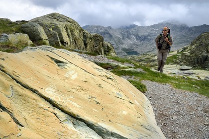 France, Alpes-Maritimes, parc national du Mercantour (Mercantour National Park), the Vallee des Merveilles (Valley of Wonders) scattered with thousands of rupestral engravings of the Bronze Age, Pas de l'Arpette (Arpette pass), hiker approaching the engraving called the zigzag arm Anthropomorphous, a checkerboard-like figure that could symbolize cultivated fields left and two daggers