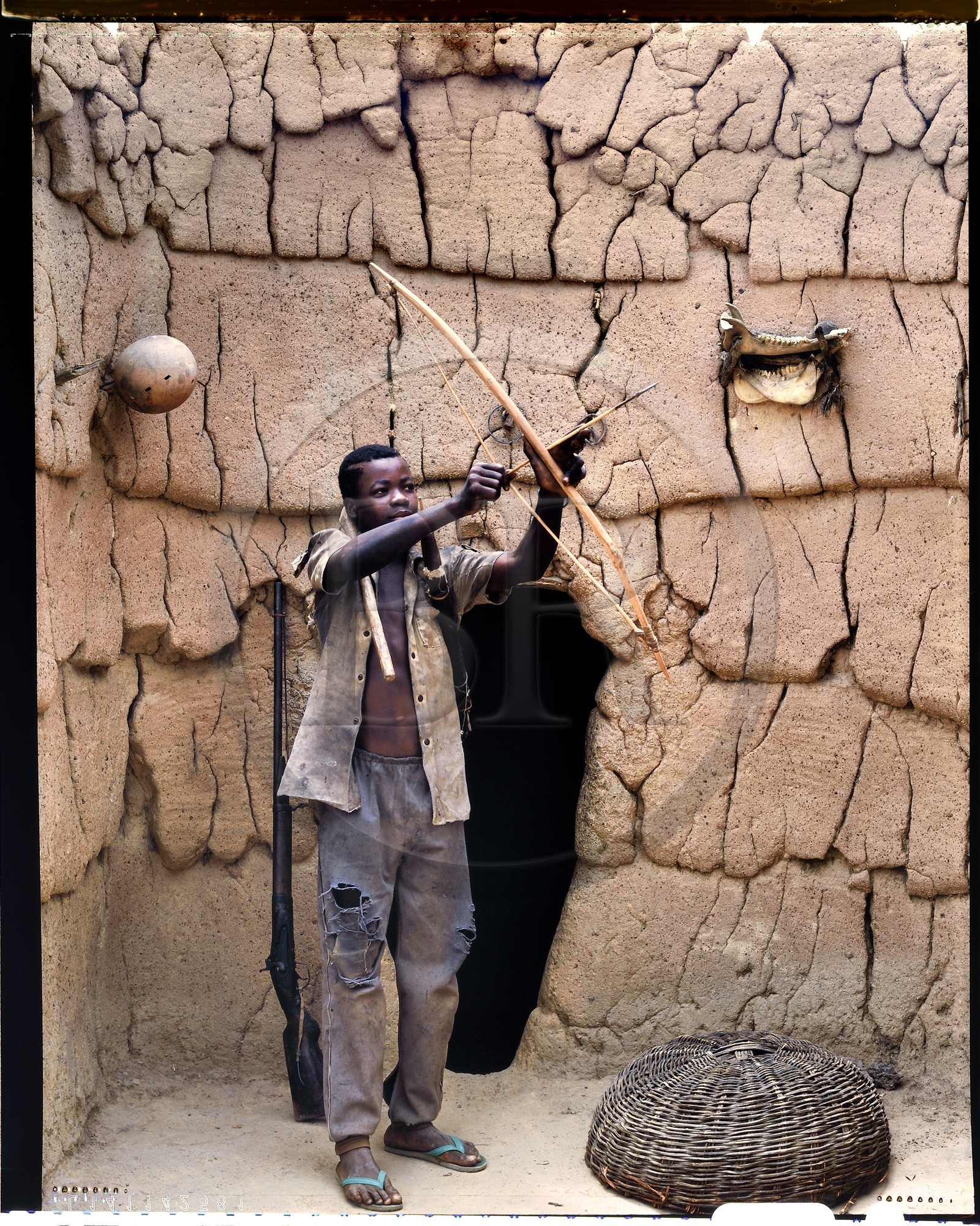 Burkina Faso, province de Poni, pays des Lobi, Loropéni, jeune Lobi devant la maison de son père avec les attributs des initiés: l'arc, le carquois et la houe