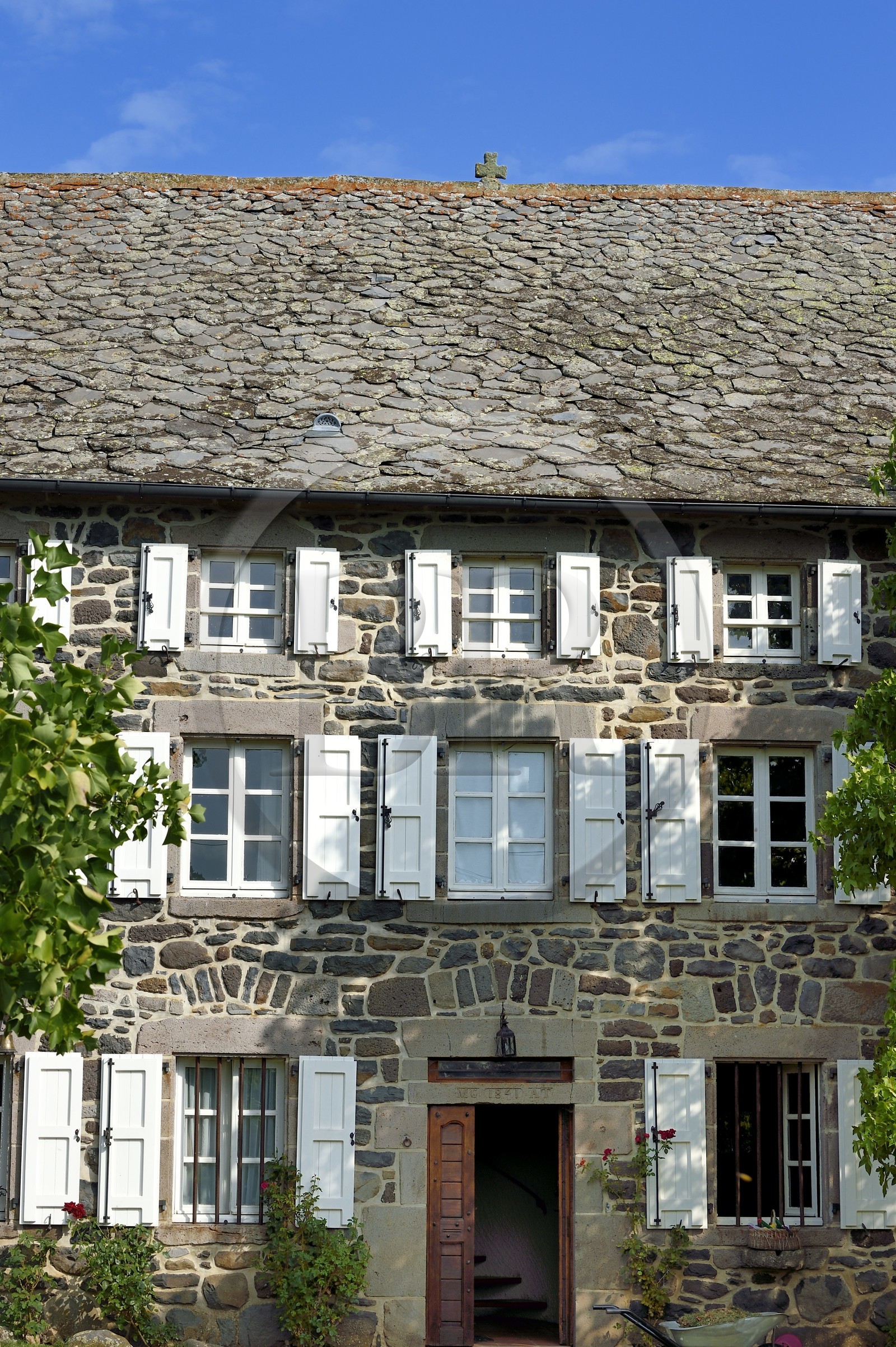 France, Cantal (15), Parc Naturel Régional des Volcans d'Auvergne, étape sur le chemin de Saint-Jacques de Compostelle par la Via Arverna, Chalinargues, hameau de Mons, la croix en pierre surmontant le toit des maisons couvertes en lauze est l’un des grands thèmes traditionnels de protection