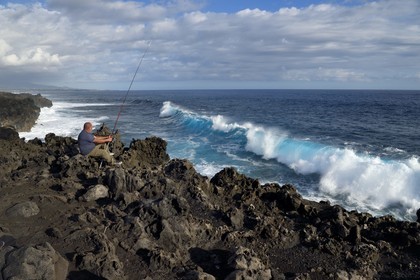 France, Ile de la Reunion, L'Etang Salé les Bains, la côte entre Le Gouffre et l'Etang du Gol, roches noires basaltiques d'origine volcanique tourmentées par l'océan, pêcheur à la ligne