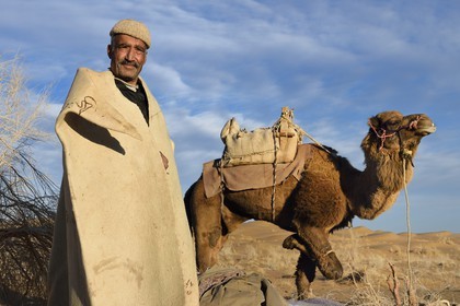 Iran, Province d'Ispahan, désert du Dasht-e Kavir, Mesr dans la région de Khur et Biabanak, le chamelier Ali Saraban portant le feutre en laine de chameau (namad) de son grand-père et un de ses dromadaires au bivouac de Kuh e-Sefid