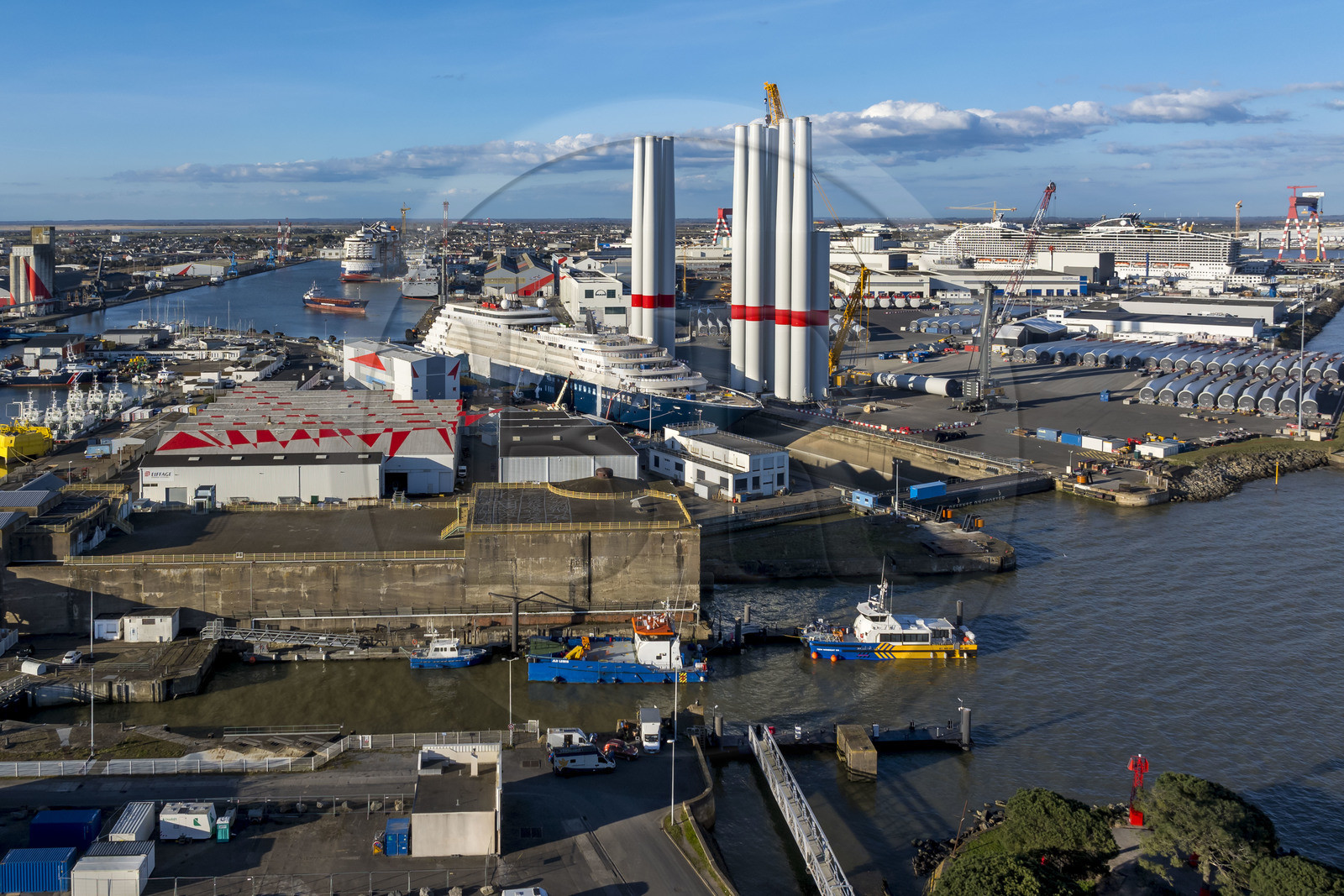 France, Loire Atlantique, Saint Nazaire, the East lock and the fortified lock of the former German submarine base built during the last world war in the foreground and the construction site of the luxury super-yacht Ritz-Carlton Luminara in the Joubert dry dock, the wind turbine towers  on the right are stored before embarkation, the 333m MSC World America cruise ship built by Chantiers de l'Atlantique in the background (aerial view)