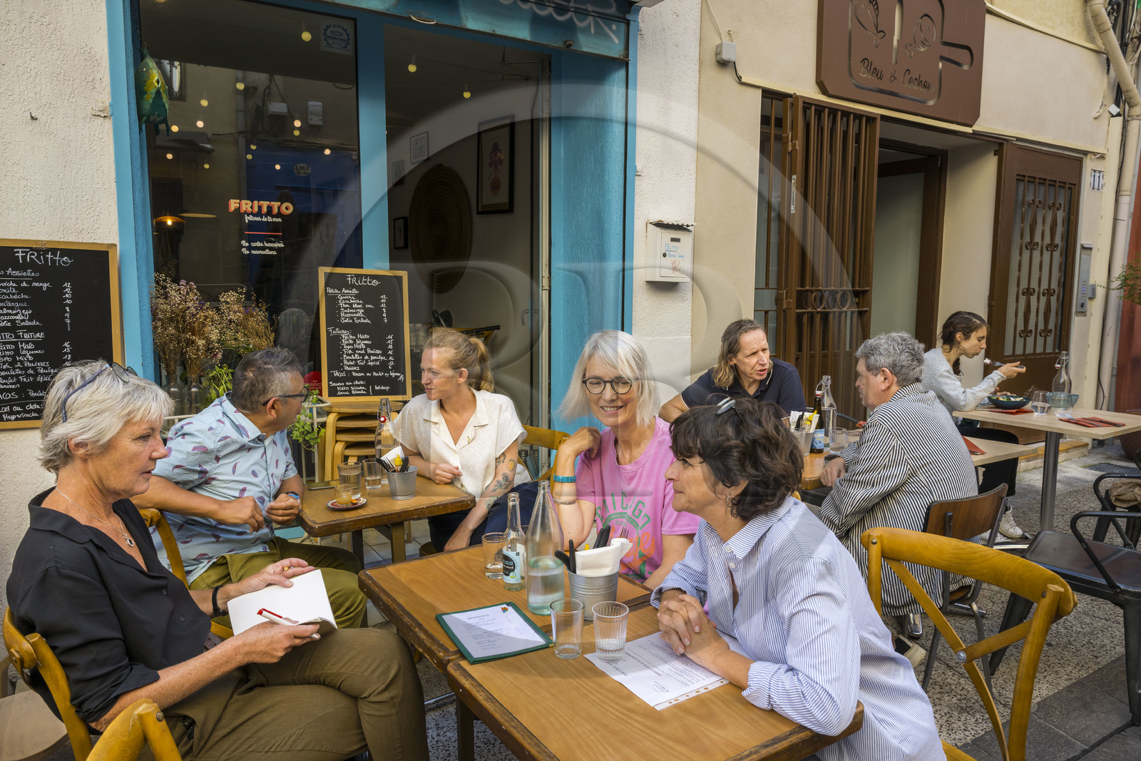 France, Hérault (34), Sète, restaurant Fritto rue André Portes, l’artiste sétois Topolino (Marc Combas) en terrasse avec la cheffe Marilou Fassanaro à gauche et son frère l’artiste sétois Robert Combas à droite en arrière-plan
