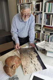 France, Paris, the french paleontologist and paleoanthropologist Yves Coppens, professor at the College de France, in the office of his home in Paris, he shows us a picture of Laetoli footprints under the watch of the supposed reproduction of Lucy's face