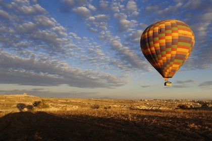 Turkey, Central Anatolia, Nevsehir Province, Cappadocia listed as World Heritage by UNESCO, hot air baloon flying over and Uchisar Rock in the background