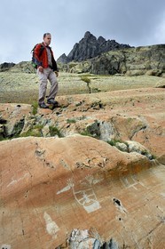 France, Alpes-Maritimes, parc national du Mercantour (Mercantour National Park), the Vallee des Merveilles (Valley of Wonders) scattered with thousands of rupestral engravings of the Bronze Age, hiker over the hornlike anthropomorphized figure engraved on the so called rock of The Sorcerer on the chiappes yellow schist flagstones