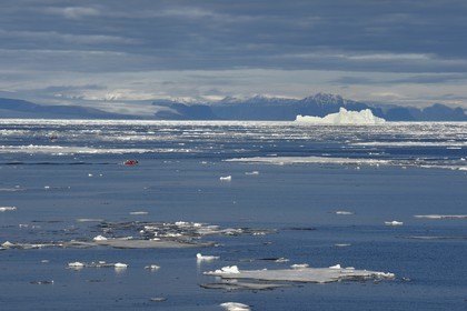 Greenland, North West coast, Smith sound north of Baffin Bay, broken pieces of Arctic sea ice and an exploration PolarCirkel boat (zodiac) of the MS Fram cruse ship from Hurtigruten, giant iceberg in the background towards the Canadian coast of Ellesmere Island in the background