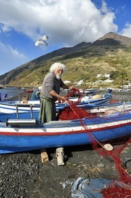 Italie, Sicile, iles Eoliennes, classées Patrimoine Mondial de l'UNESCO, ile de Stromboli, le pecheur Gaetano Cusolito réparant ses filets sur la plage de Scari et le volcan du Stromboli en arrière plan
