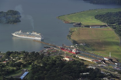 Panama, Colon province, Panama Canal, Gatun locks, Panamax cargo passing the locks, a cruise ship on Gatun Lake in the background (aerial view)