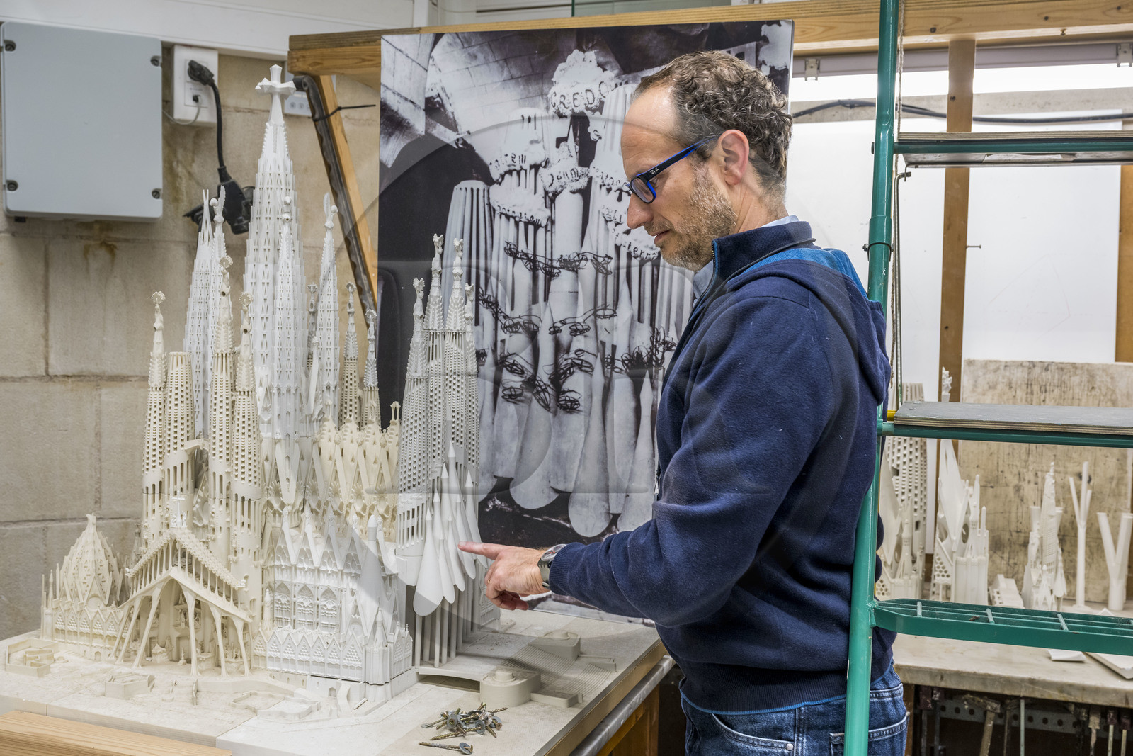Espagne, Catalogne, Barcelone, quartier de l'Eixample, basilique de la Sagrada Familia de l'architecte du modernisme catalan Antoni Gaudi classée Patrimoine Mondial de l'UNESCO, l'atelier maquettes, l'architecte et coordinateur de l'équipe des artistes et des maquettistes Jeronimo Buxareu Padros présente les prochains travaux à entreprendre, la future facade de la Gloire face à lui et la photo de la maquette originale de Gaudi en arrière plan
