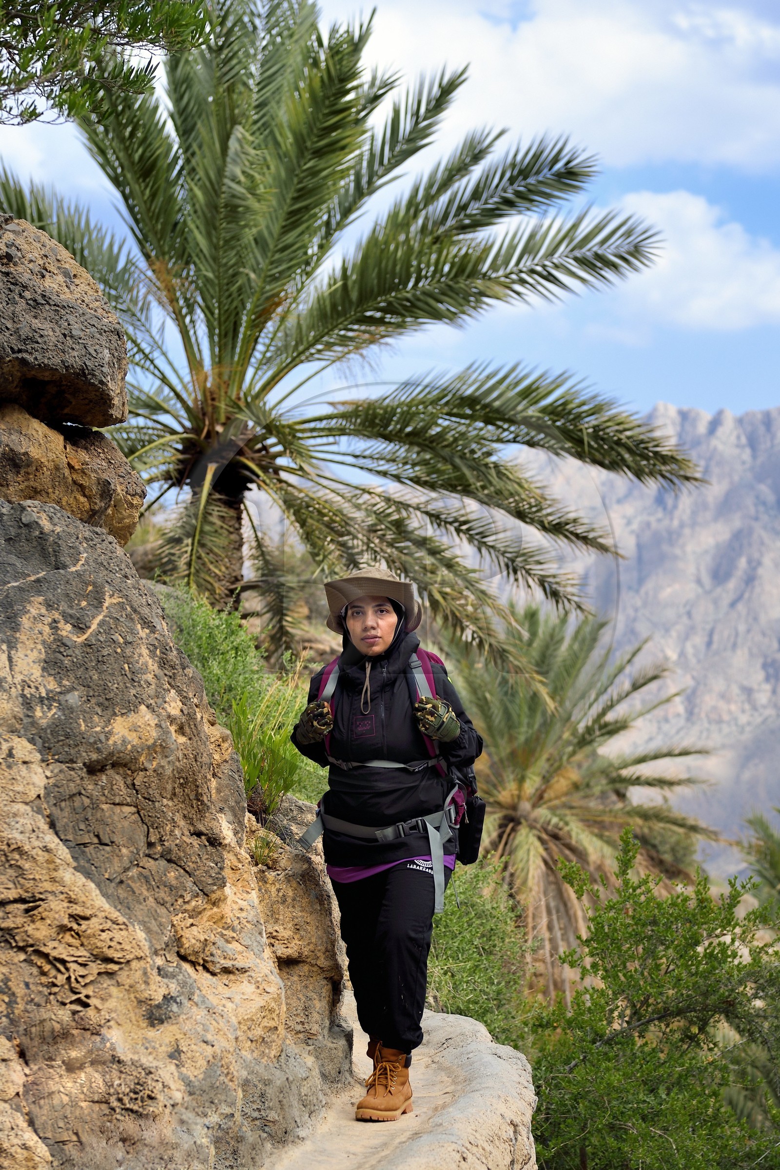 Sultanat d'Oman, Gouvernorat d'Al-Batina du Sud, Hajar occidental, Wadi Mistall, la randonneuse Badour Al Salhi suivant un falaj canal d'irrigation au dessus du village de Wakan (Wukan)