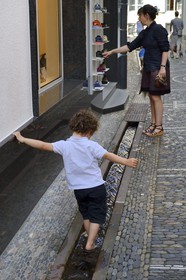 Germany, Baden-Wurttemberg, Freiburg im Breisgau, child playing in one of the Bächle which are small open channel lining the sidewalks
