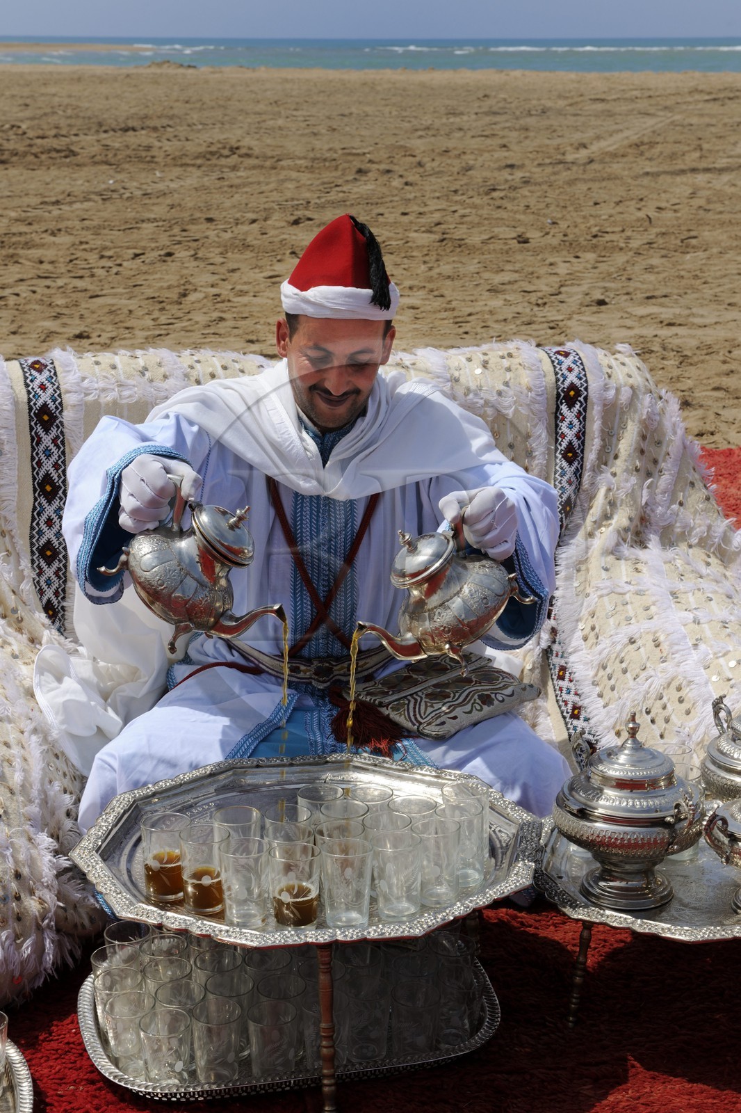 Morocco, Oriental Region, man in ceremonial cloth serving mint tea on the beach