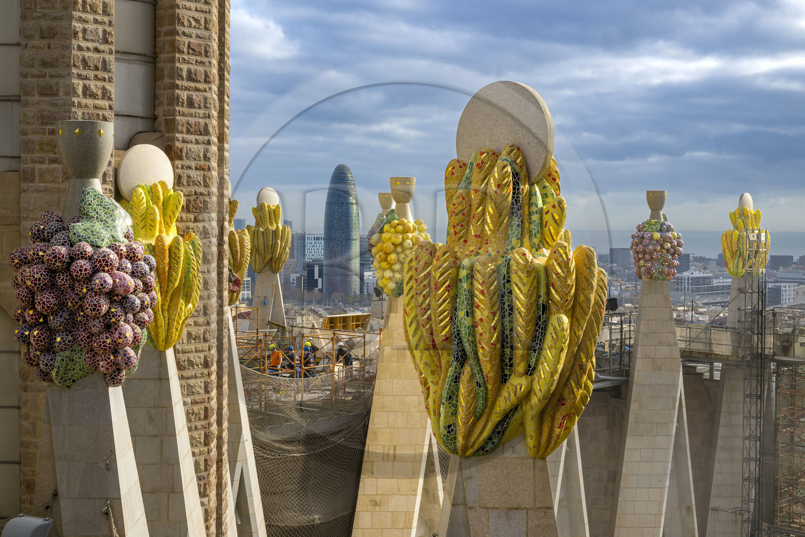 Espagne, Catalogne, Barcelone, quartier de l'Eixample, basilique de la Sagrada Familia de l'architecte du modernisme catalan Antoni Gaudi classée Patrimoine Mondial de l'UNESCO, sommets surmontés de mosaïques en forme de fruits entourant le chantier sur le toit de la nef à l'arrière de la future facade de la Gloire, la Torre Agbar de l'architecte Jean Nouvel en arrière plan