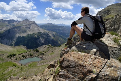 France, Alpes-de-Haute-Provence (04), Uvernet-Fours, parc national du Mercantour, vallée de l'Ubaye, sentier de randonnée du circuit des lacs du col de la Cayolle au Pas du Lausson, François Breton garde moniteur du parc assis sur une borne gravée sur les rochers délimitant la frontière entre le duché de Savoie et le comté de Nice, la vallée du Haut-Var et lac du Lausson (Alpes-Maritimes) en arrière plan